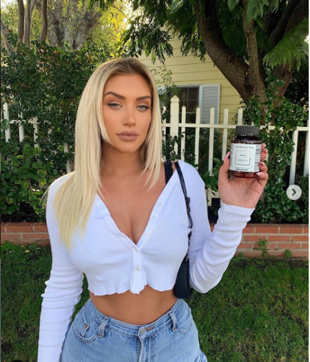 stassie wearing a white top blue jeans holding up a essential oil 